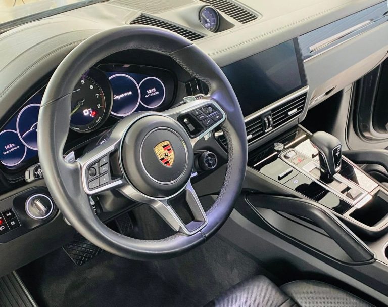 Intérieur d'une voiture de sport avec volant Porsche et tableau de bord numérique.